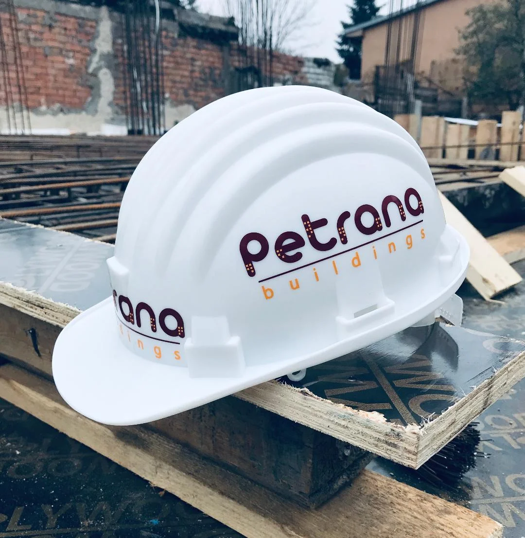 Cască de protecție personalizată cu logoul Petrana Buildings, realizat de Pixlab, prezentată pe un șantier de construcții